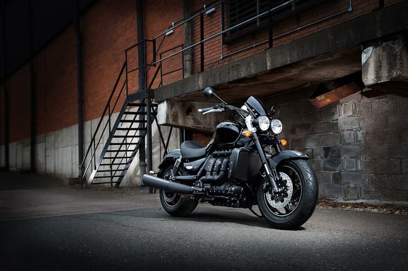 Black Triumph Rocket 3 motorcycle parked in front of an industrial brick building with cinematic lighting.