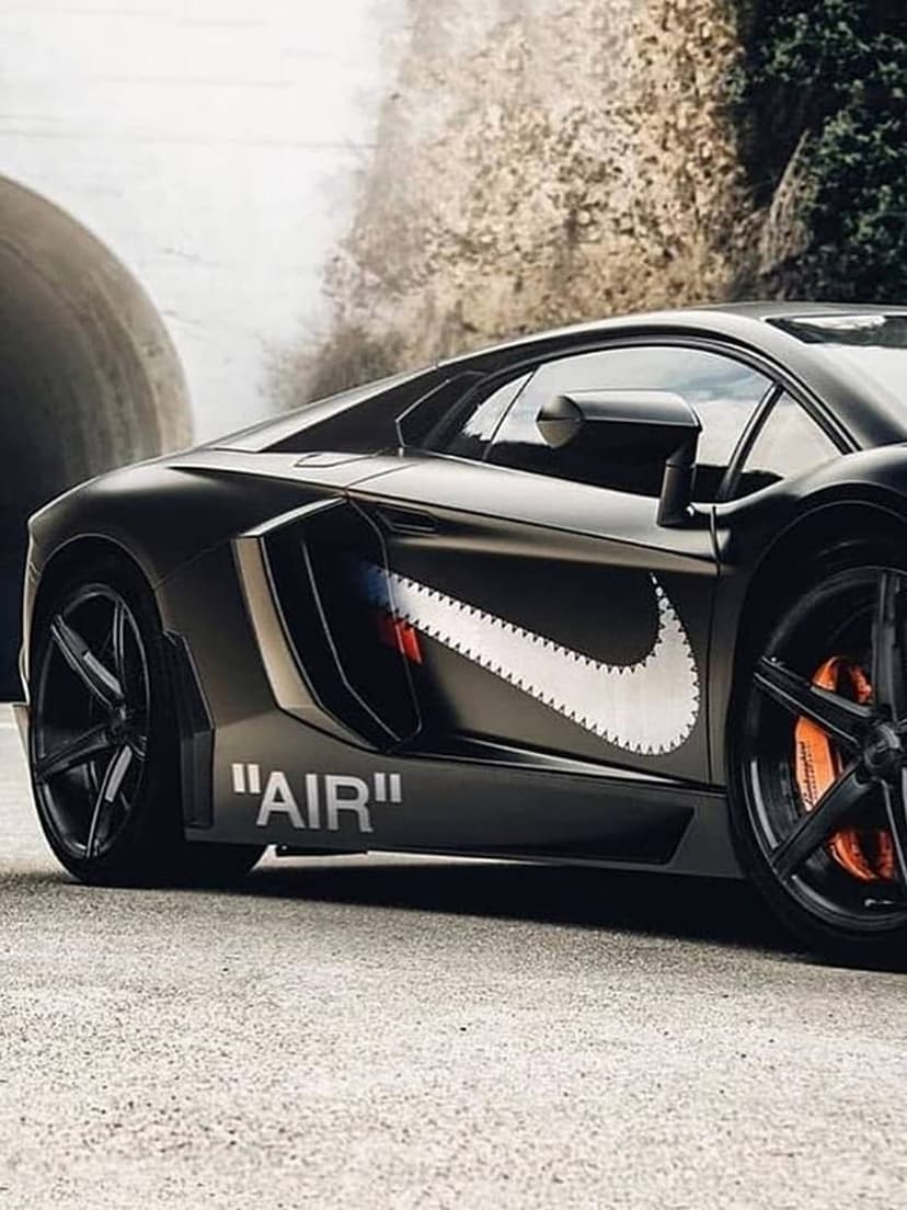 Black Lamborghini Aventador with a Nike swoosh decal and orange calipers parked near a stone tunnel entrance.