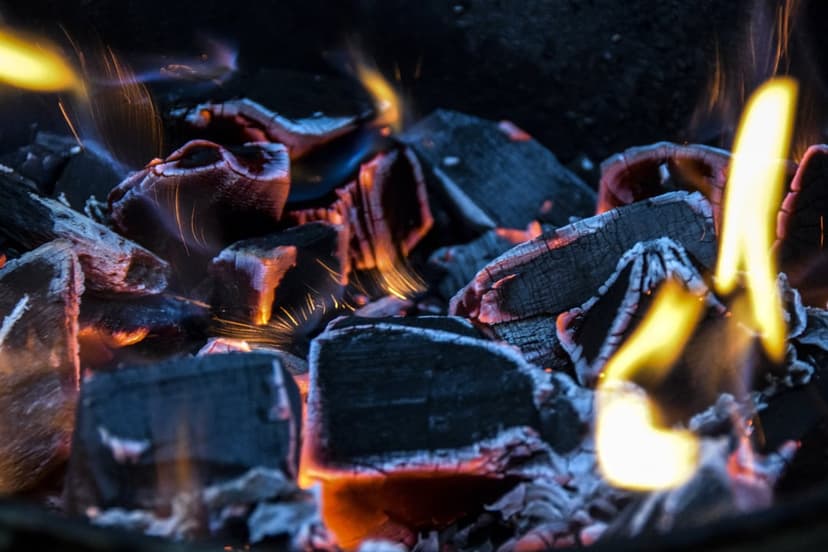 Glowing orange charcoal embers with small yellow flames and tiny sparks dancing against a dark background.