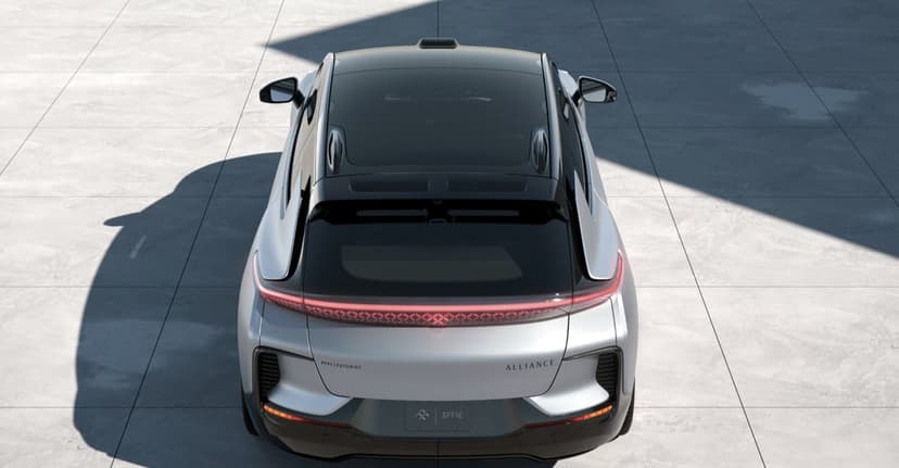Rear view of a silver futuristic SUV with a glowing red LED light bar on a grey tiled floor with sharp shadows.