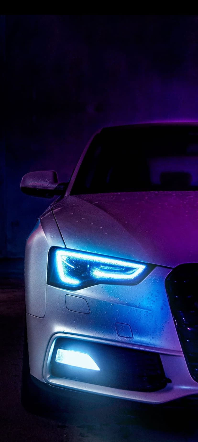 Car headlights glowing with blue and purple neon light feature realistic water droplets on a dark metal surface.
