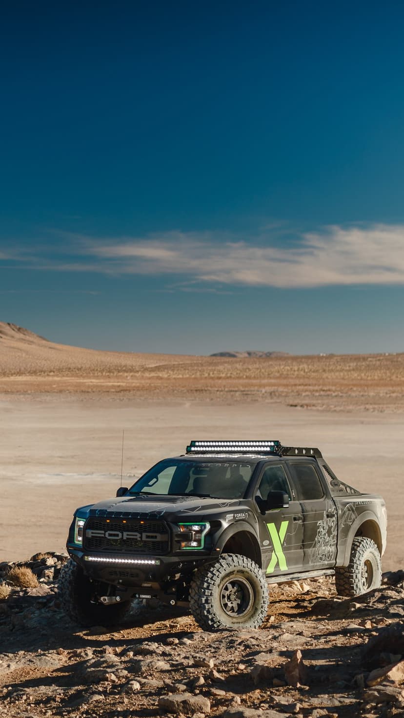Modified Ford Raptor with neon green accents and roof lights parked on rocky desert terrain under a blue sky.
