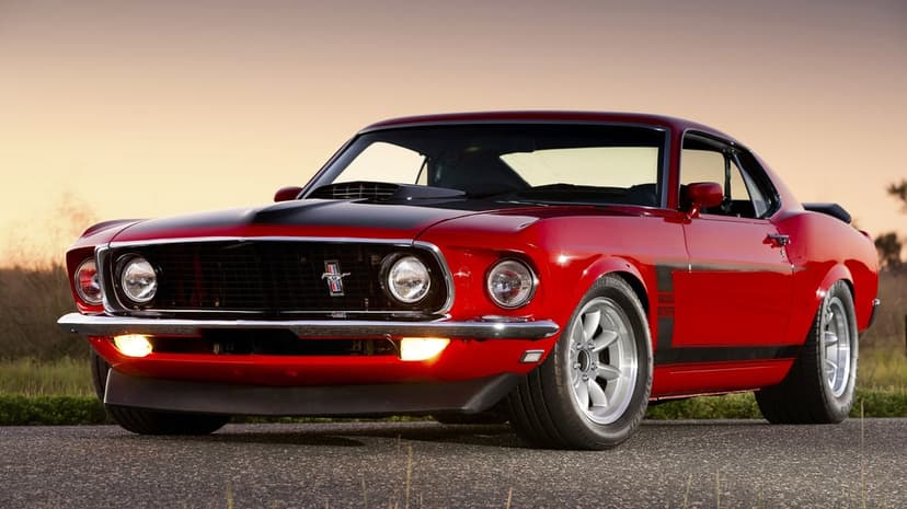 Red 1969 Ford Mustang Boss 302 on a road at sunset with glowing fog lights, black hood, and silver wheels.