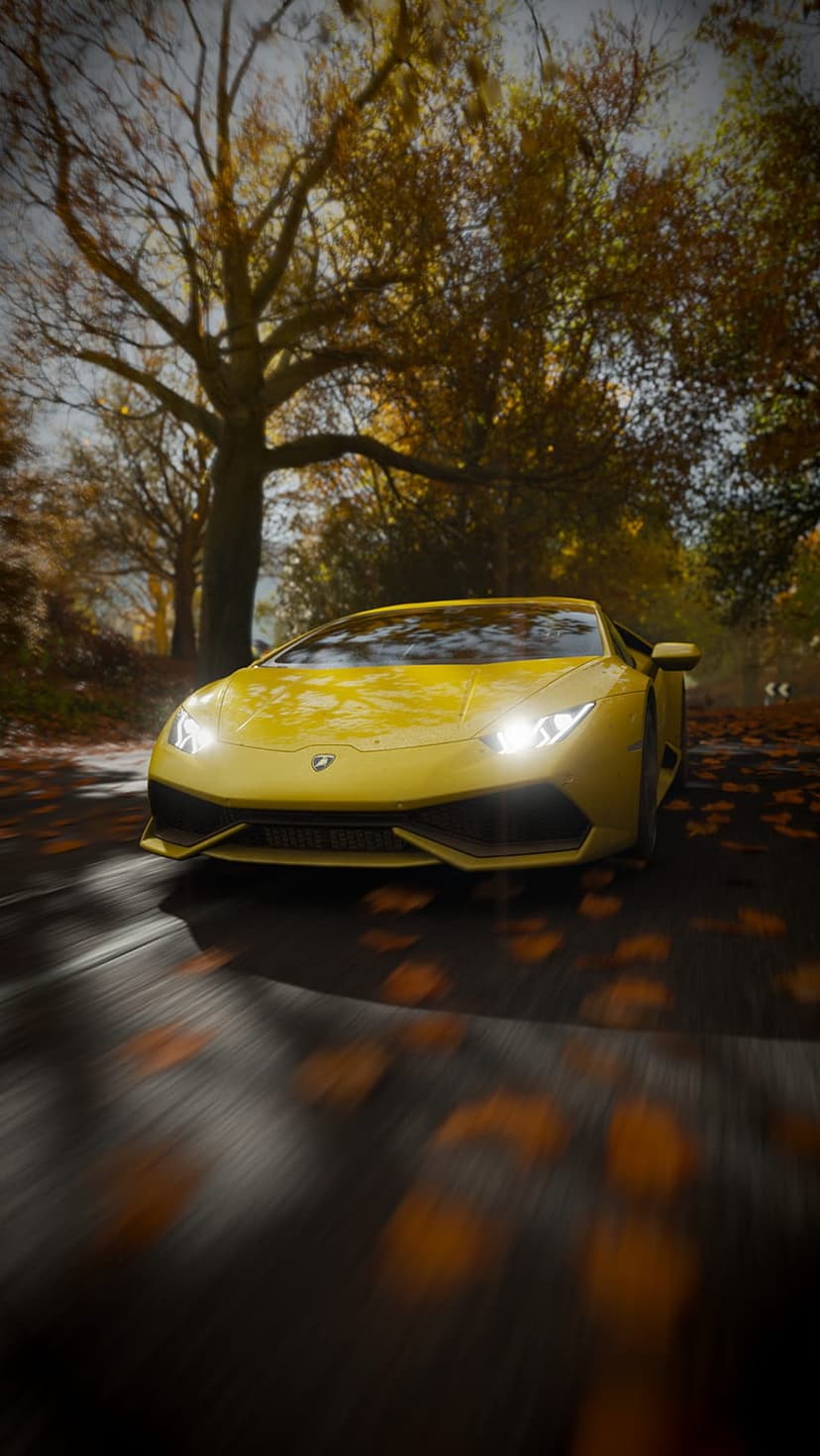 Yellow Lamborghini supercar driving fast on a forest road covered in orange autumn leaves with motion blur.