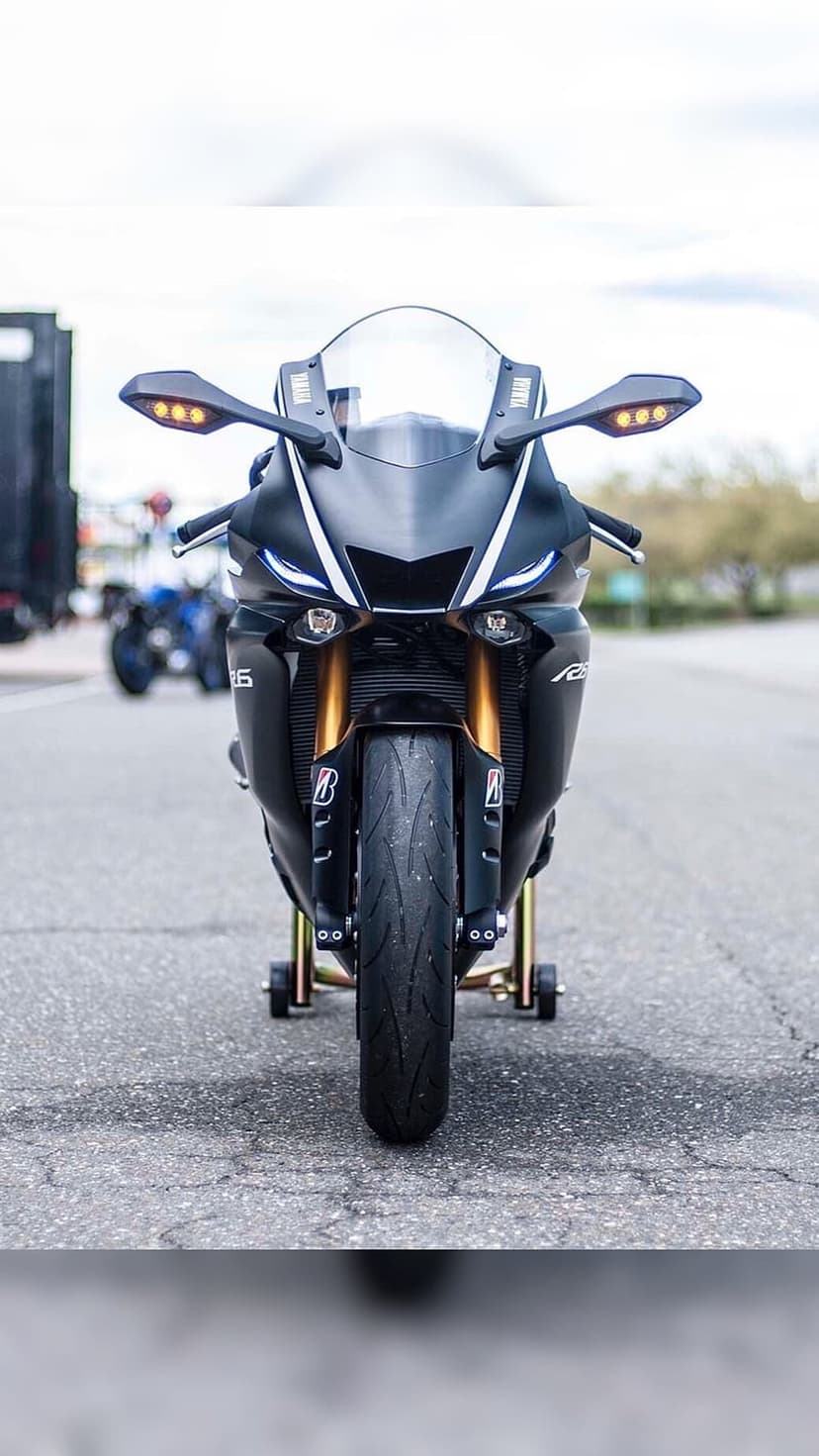 Black Yamaha R6 motorcycle with gold forks and LED headlights rests on a yellow paddock stand on asphalt.
