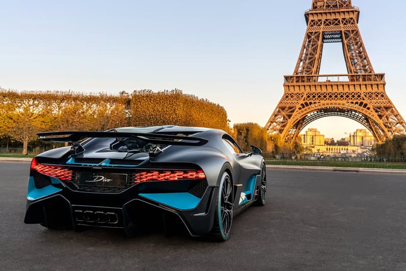 Bugatti Divo supercar in matte grey with blue accents parked near the Eiffel Tower in Paris at sunset.