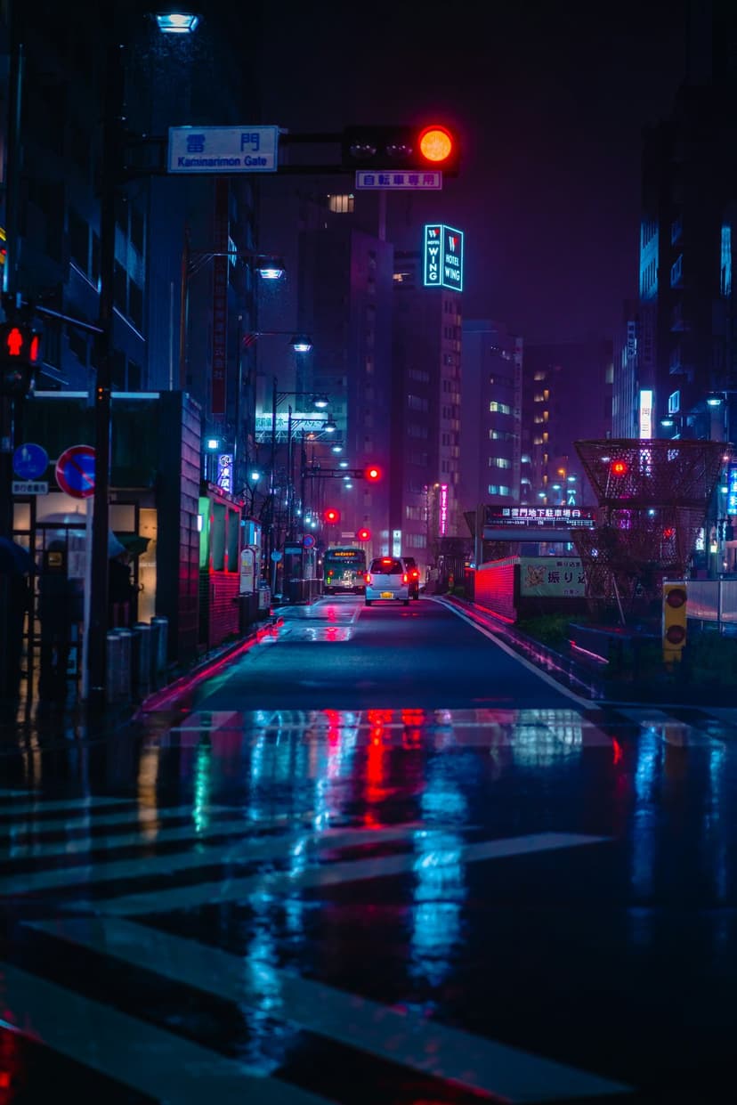 Wet Tokyo street at night with glowing neon signs reflecting on asphalt as a bus and cars drive through rain.