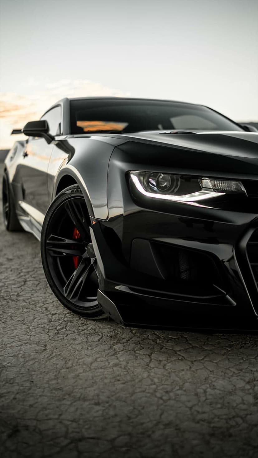 Black Chevrolet Camaro ZL1 with red brake calipers parked on dry, cracked earth under a soft, hazy sky.