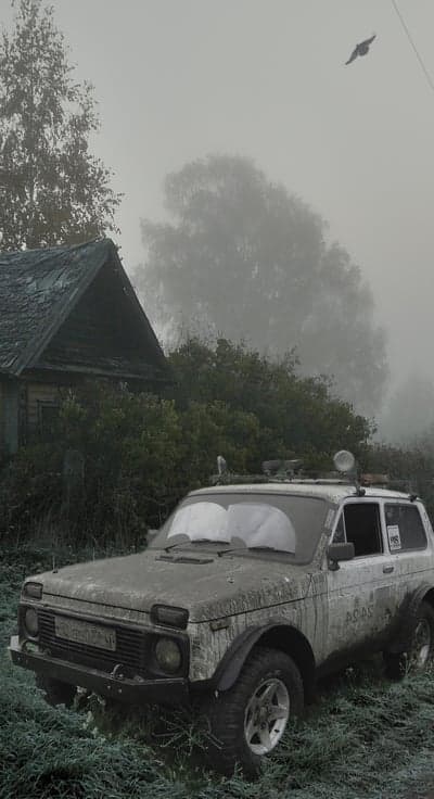 Mud-covered SUV parked by old house in foggy landscape