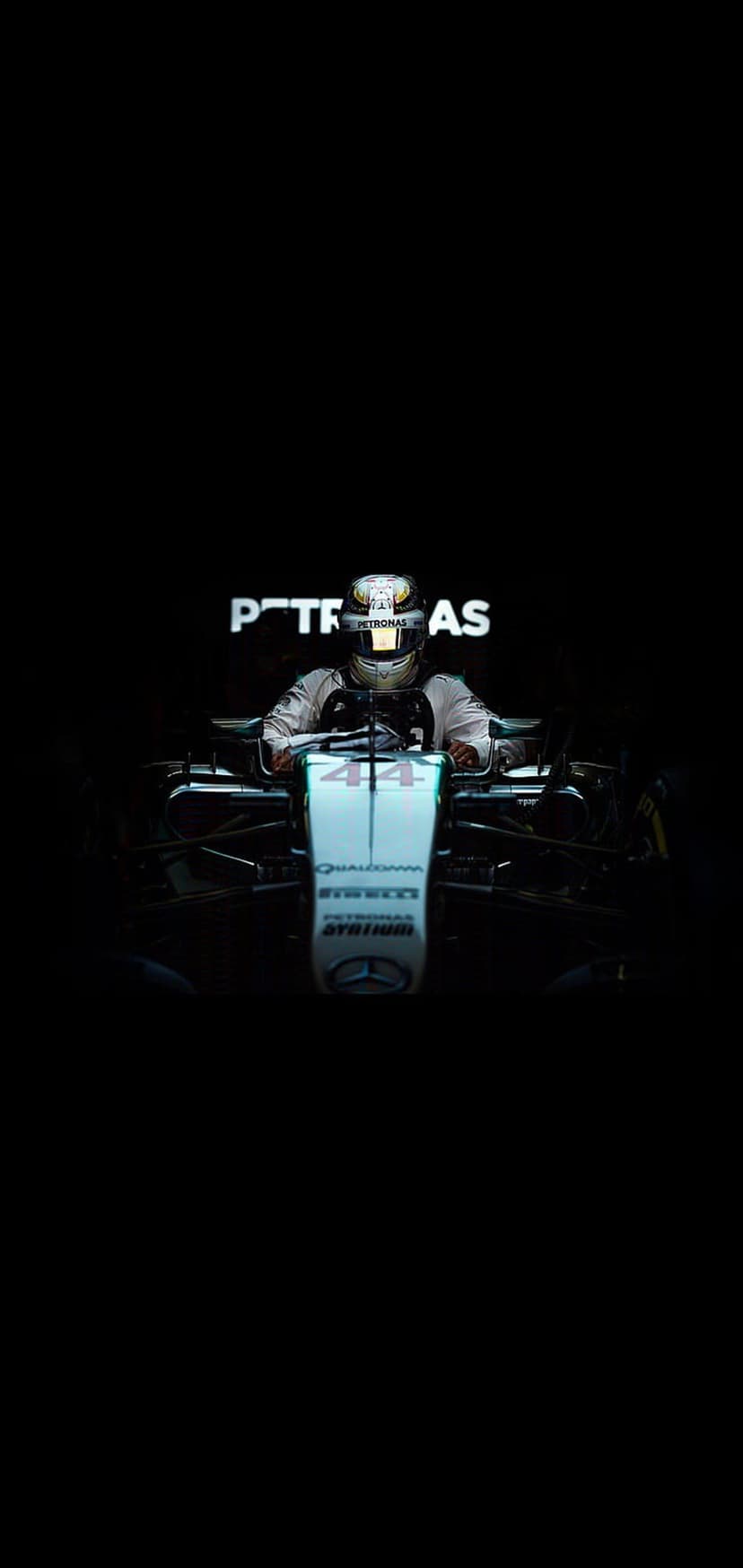 Formula 1 driver in a Mercedes racing suit and helmet sits inside a cockpit with number 44 and Petronas branding.