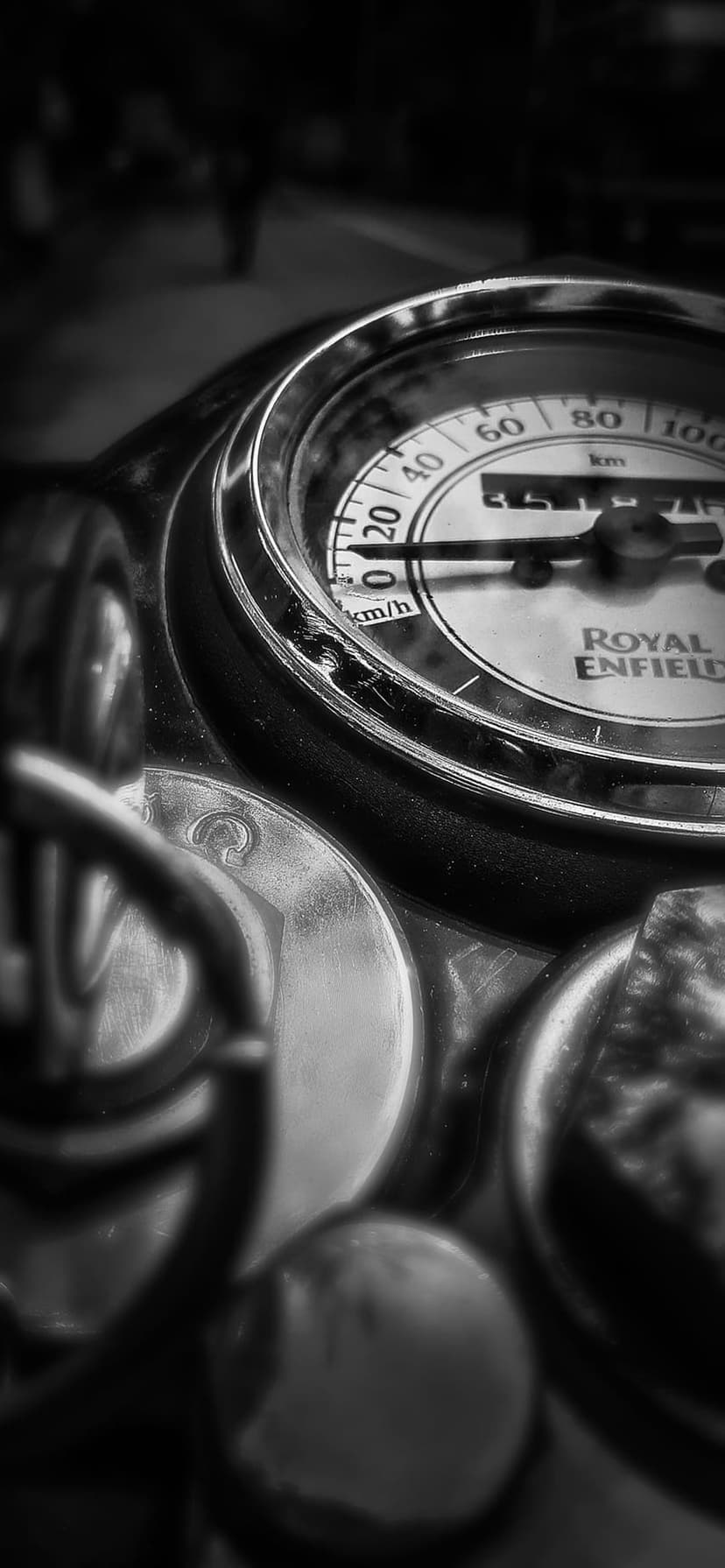 Royal Enfield speedometer showing km/h alongside polished chrome handlebars in a high-contrast monochrome view.