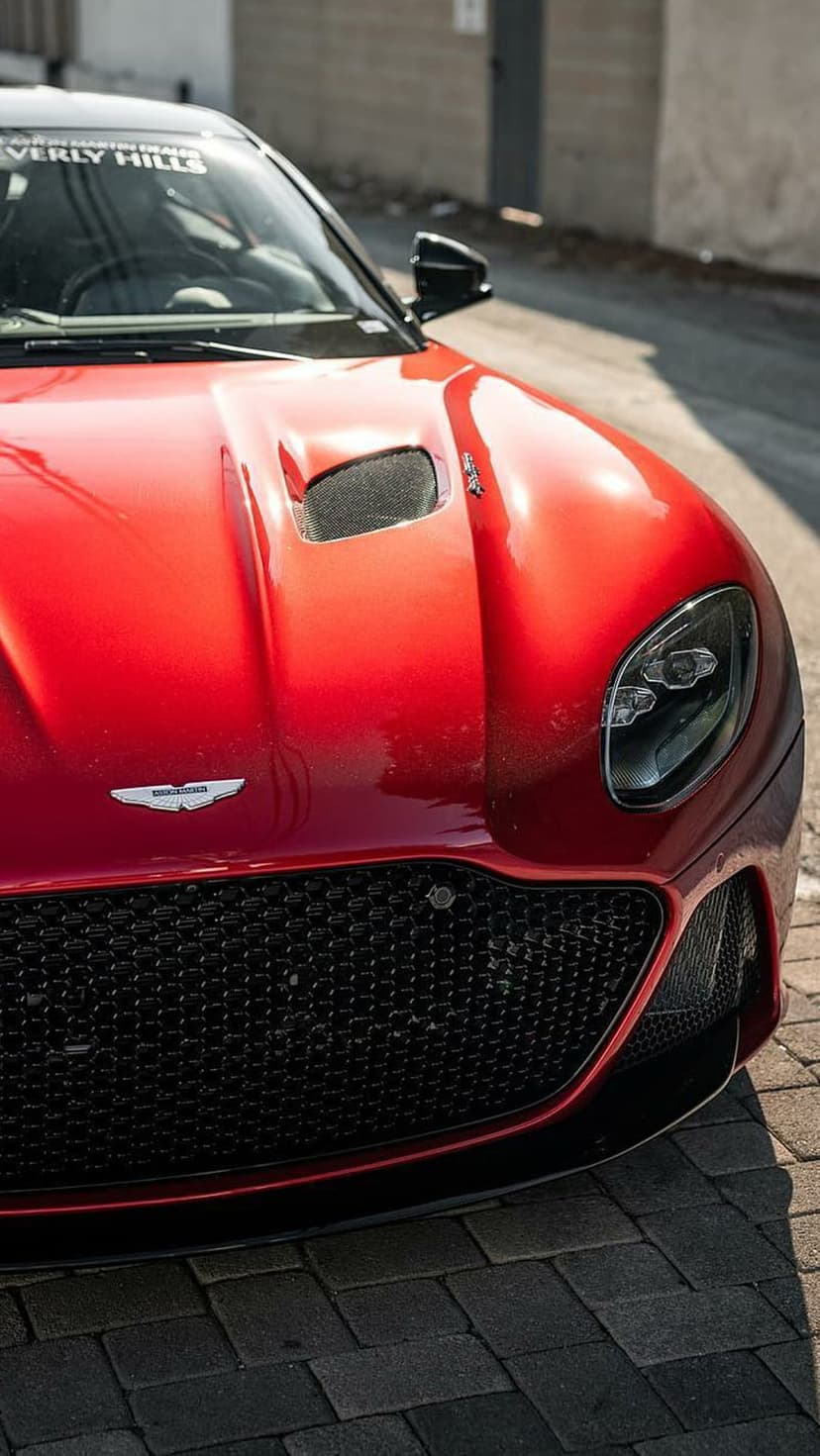 Red Aston Martin DBS Superleggera front view with a black grille on a brick road for a mobile screen background.