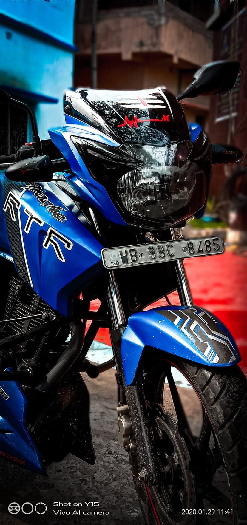 Blue Apache RTR motorcycle front view showing sharp headlights and a red heartbeat decal on the black visor.