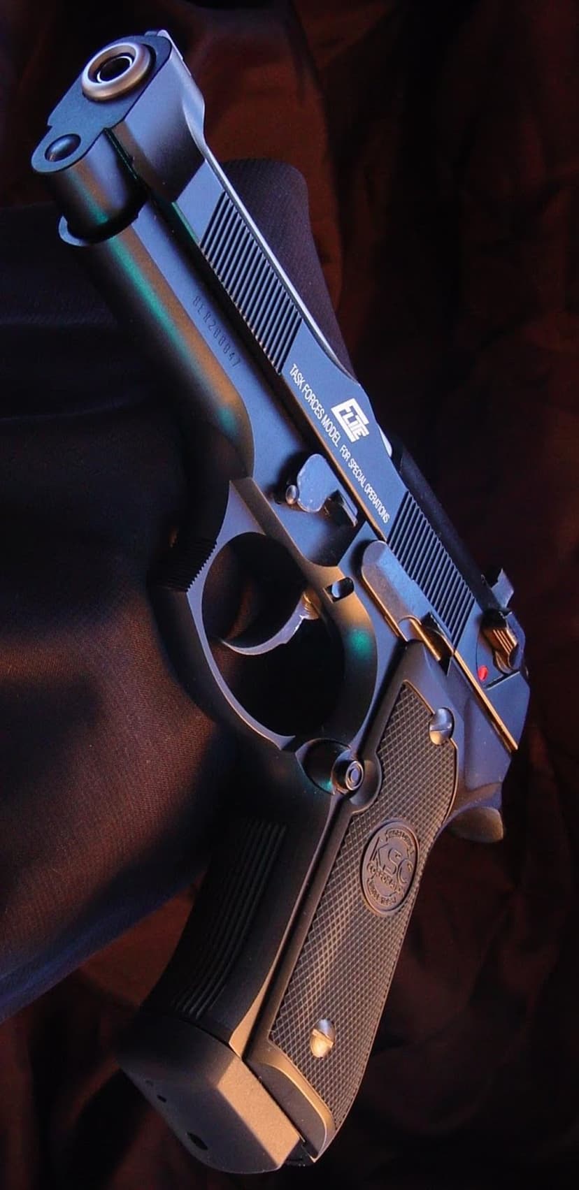 Black tactical handgun with a textured grip and serrated slide, showcasing special operations markings in a close-up.