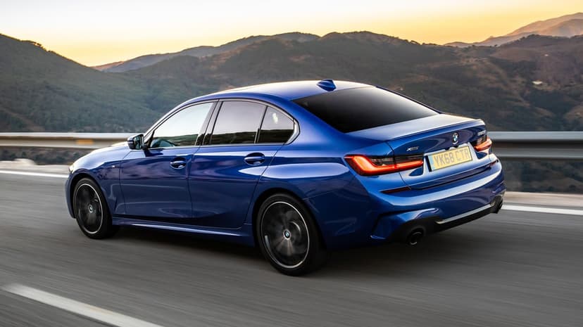 Blue BMW sedan driving on a mountain road during sunset with motion-blurred wheels and golden hour lighting.
