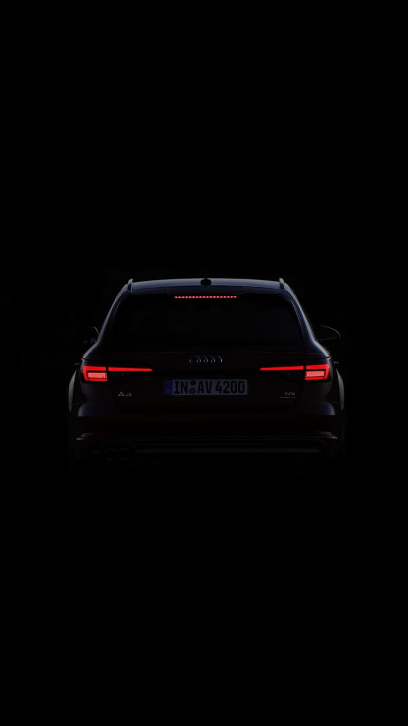 Audi A4 Avant rear LED taillights and brake lights glow bright red against a dark, shadowy car silhouette.