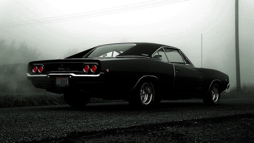 Black classic muscle car with glowing red tail lights parked on a misty road during a foggy day.