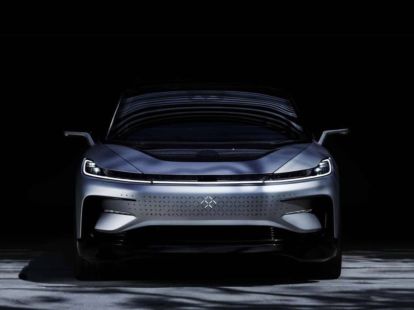 Front view of a sleek silver electric car with slim LED headlights and diamond-patterned grille on a black backdrop.
