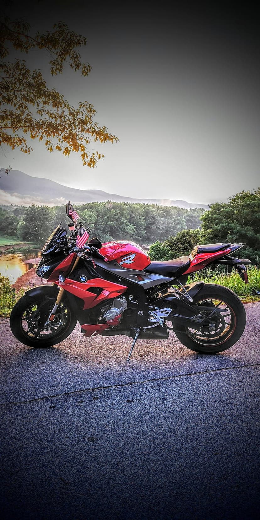 Red BMW motorcycle parked on a road with American flags, overlooking a green valley and misty mountain peaks.