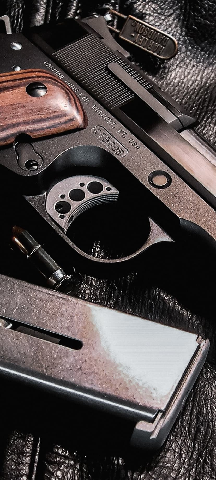 Harley Davidson handgun featuring a wood grip and engraved slide sits beside a loaded magazine and brass bullet.