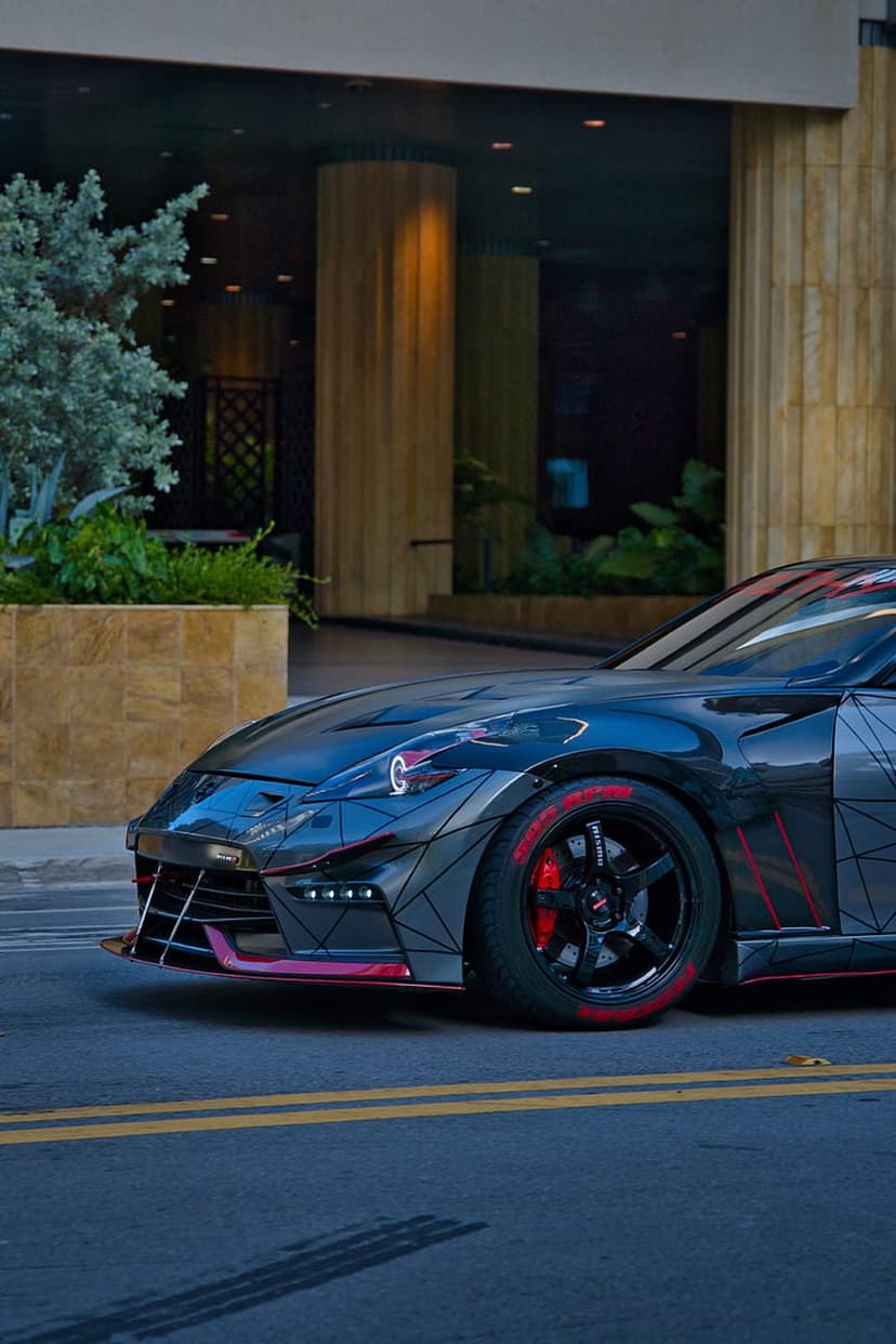 Custom sports car with red accents and a wide body kit parked on a city street beside modern glass architecture.