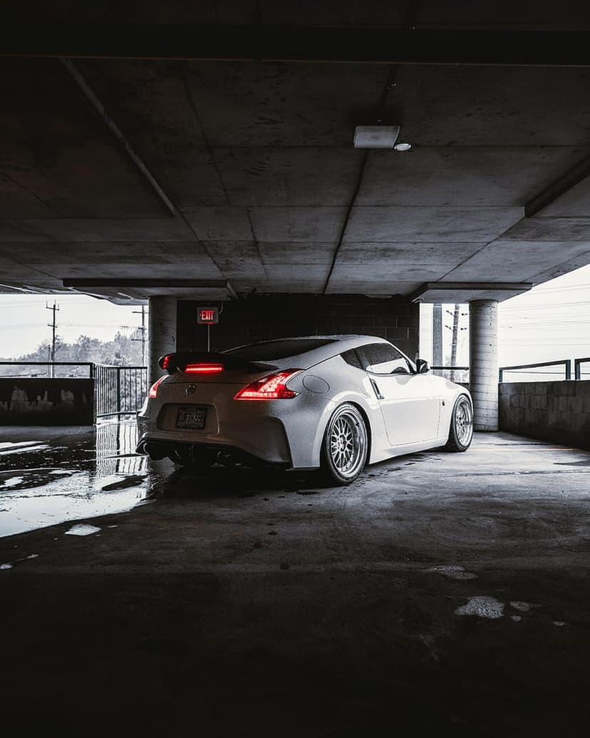 White Nissan 370Z sports car parked in a dark concrete garage with glowing red taillights and floor reflections.