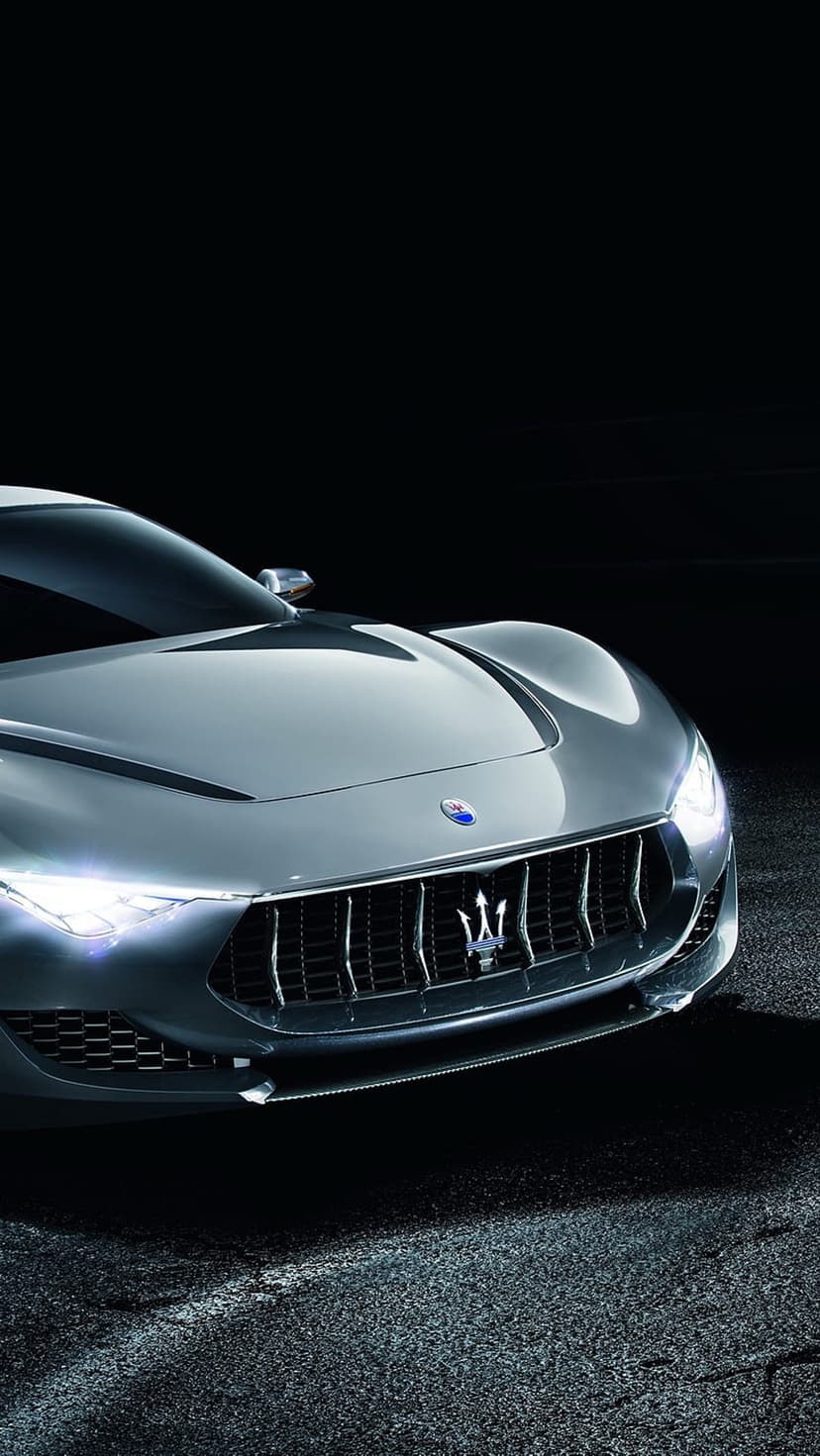 Maserati GranTurismo concept car front grille with a silver trident emblem and glowing LED headlights on asphalt.