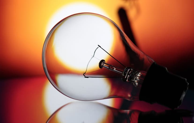 Clear light bulb reflecting orange sunset light on a dark surface with a visible glowing metal filament inside.