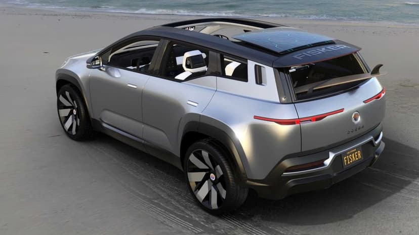 Silver Fisker Ocean electric SUV on a sandy beach with an open solar roof and ocean waves in the background.