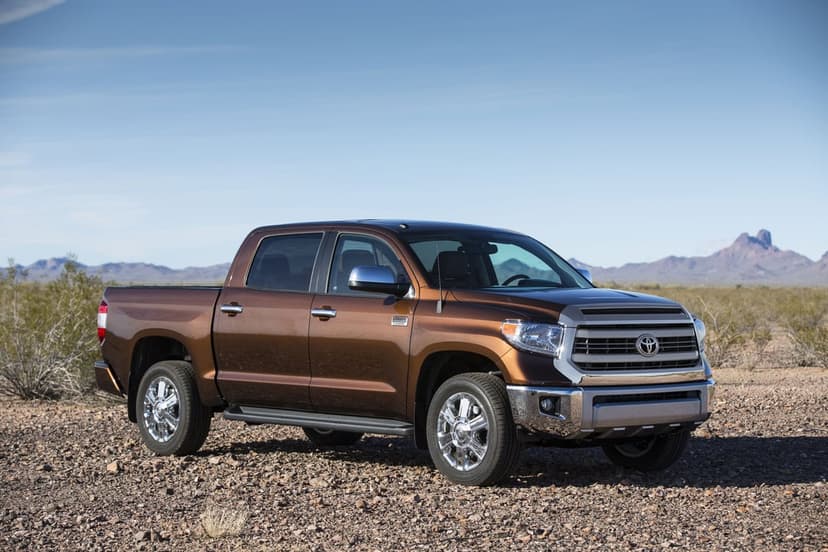 Brown Toyota Tundra pickup truck parked on rocky desert ground with mountains under a clear blue sky.