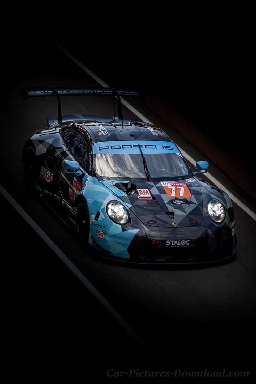 Porsche 911 RSR race car with blue and grey camouflage livery number 77 driving on a track during low light.