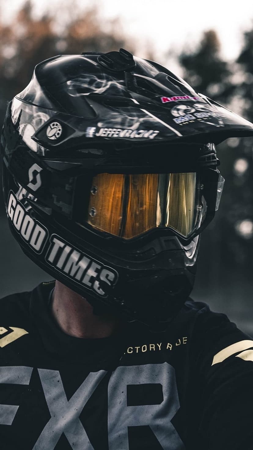 Motocross rider wearing a black helmet with gold goggles and a jersey featuring bold white lettering.