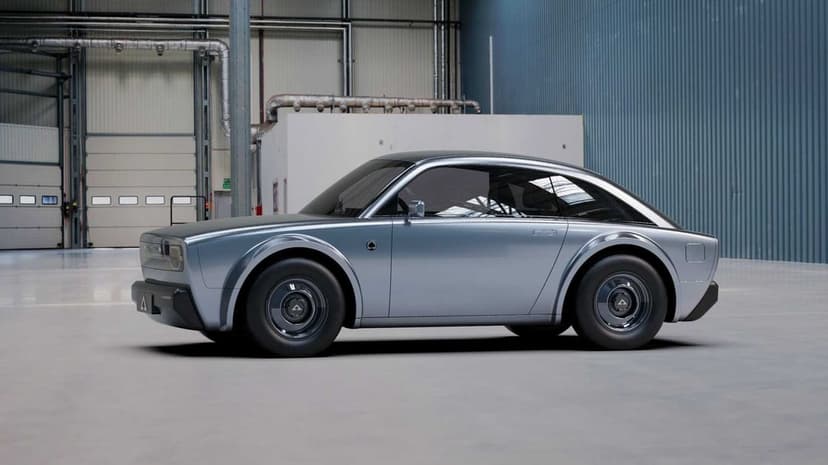 Side profile of a silver electric coupe in a blue industrial hangar with polished concrete floors and soft light.