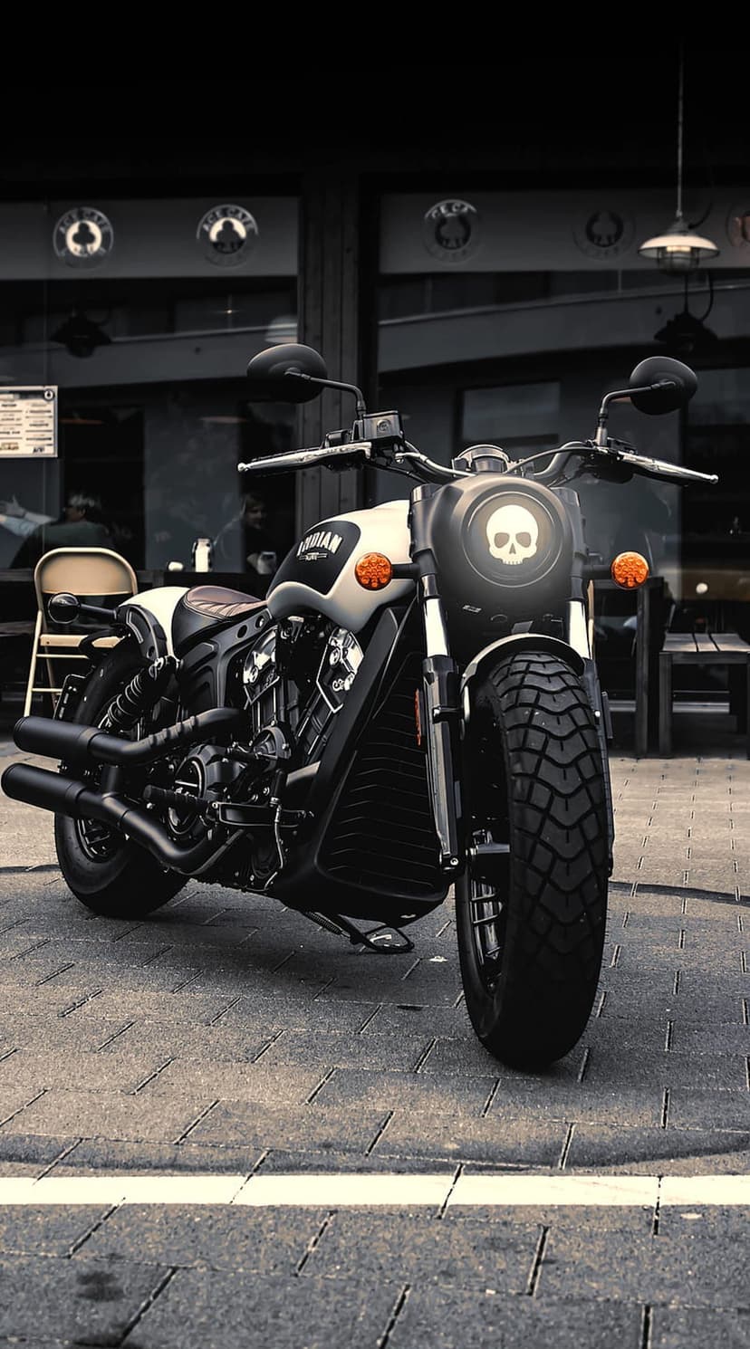 Indian motorcycle with a skull headlight and dual exhausts parked on a textured cobblestone street in grayscale.