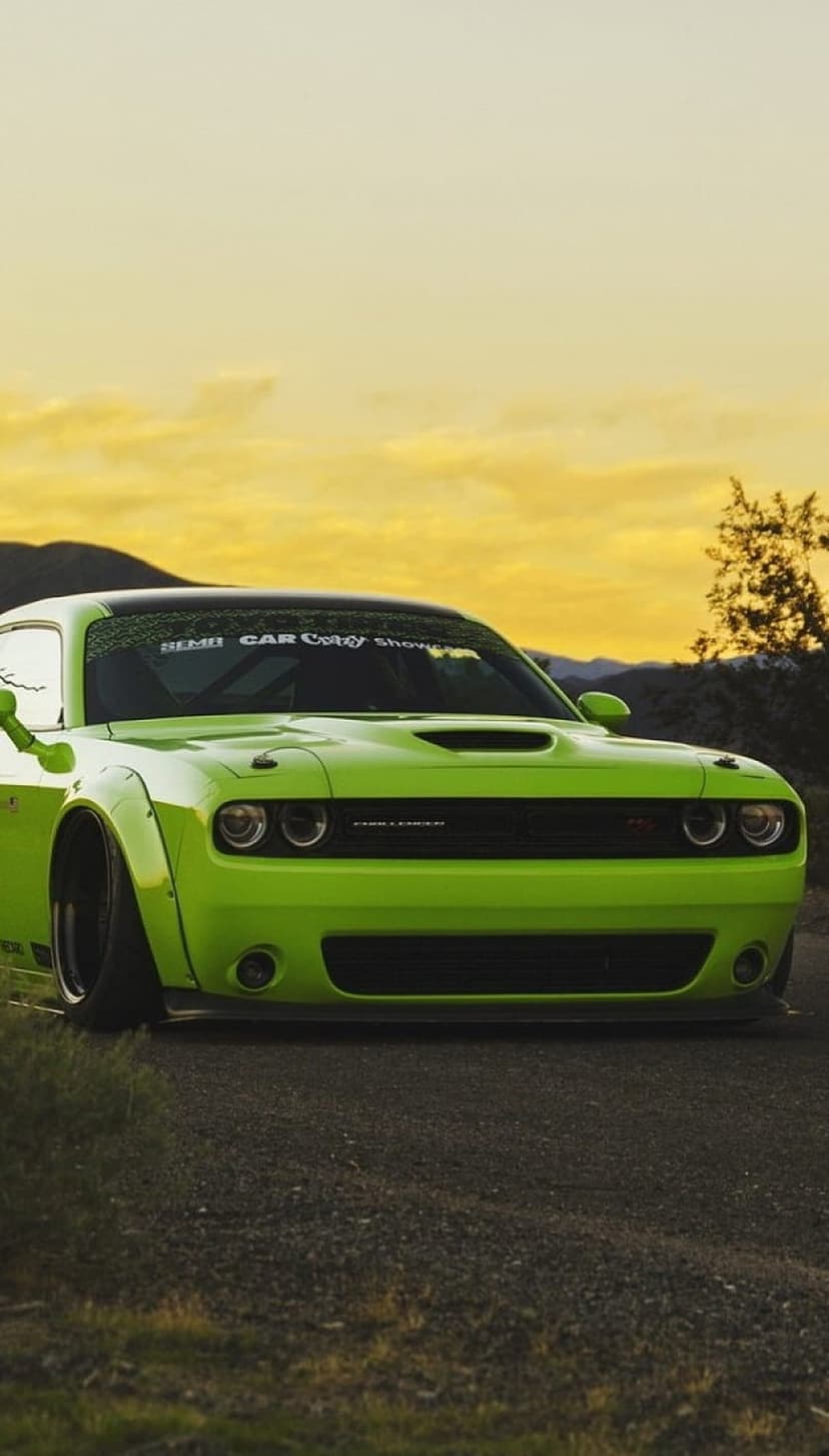 Lime green Dodge Challenger Hellcat with a widebody kit parked against a vibrant orange and yellow mountain sunset.