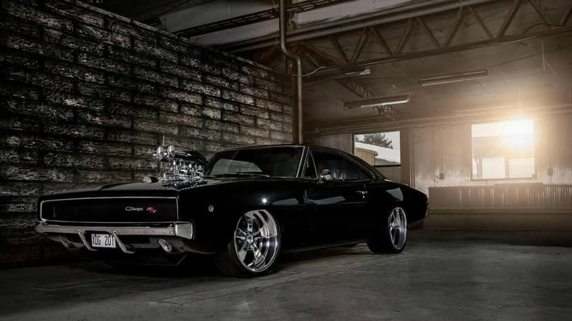 Black Dodge Charger R/T with a chrome blower and deep dish wheels in a sunlit industrial warehouse setting.