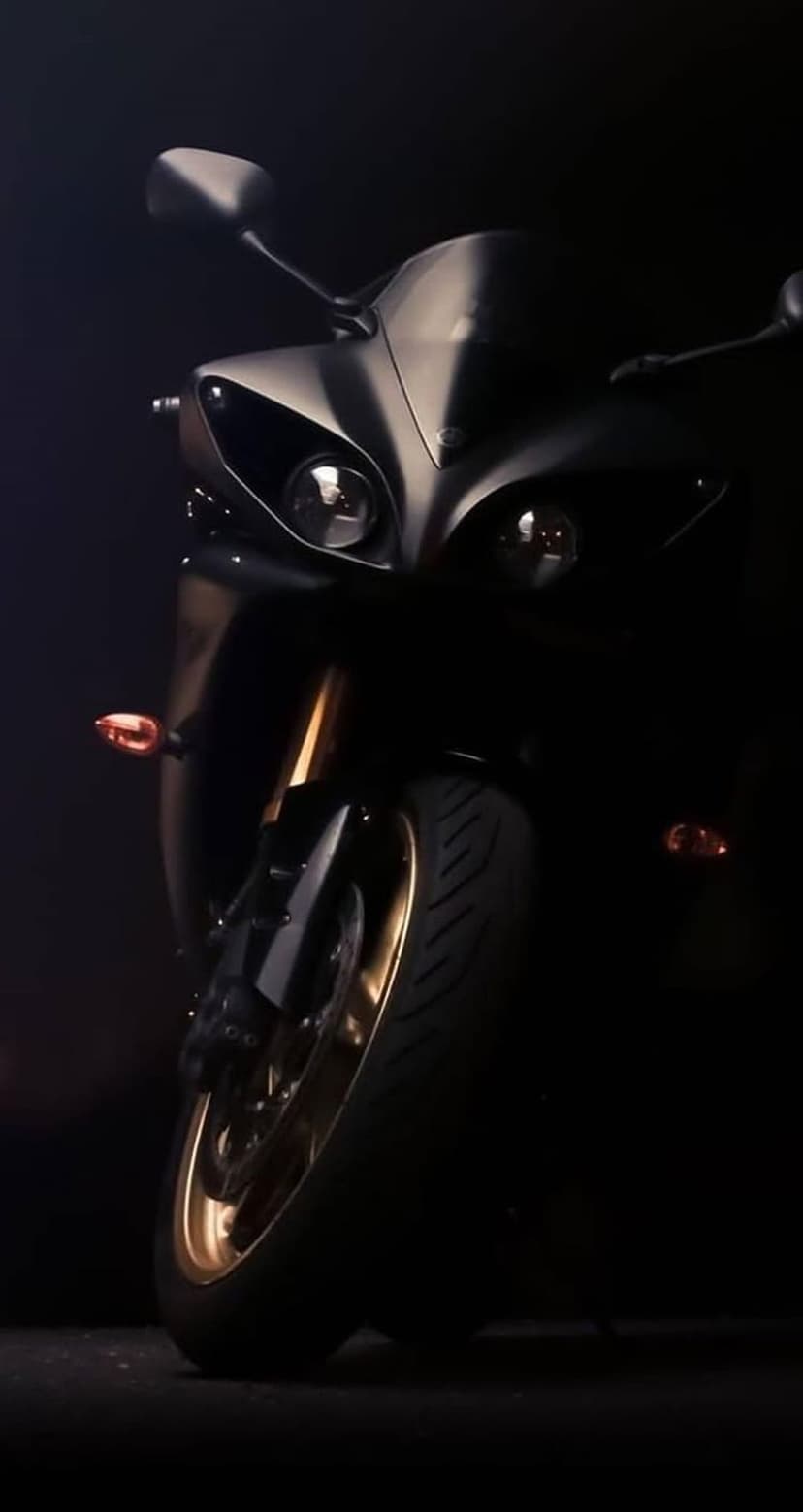 Matte black sportbike front view with glowing twin headlights and metallic gold rims in low-light conditions.