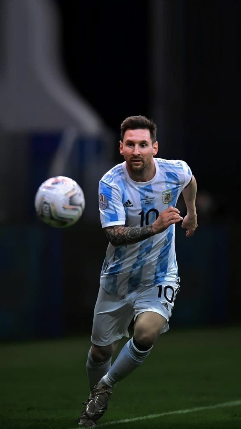Lionel Messi sprints toward a soccer ball in an Argentina jersey on a dark green field with stadium lighting.