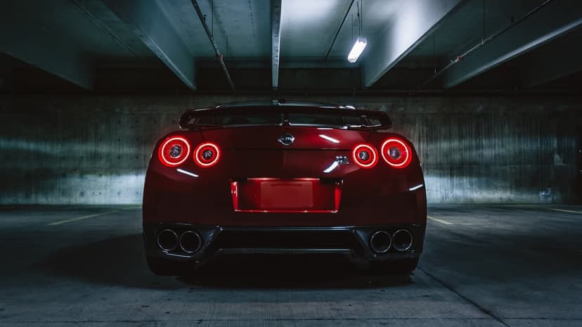 Red Nissan GT-R rear view in a concrete garage with glowing quad circular tail lights and chrome exhausts.