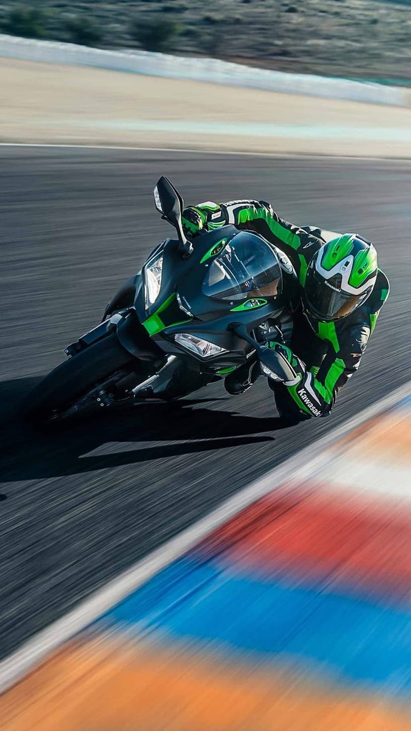 Kawasaki sportbike rider in green gear leans into a track corner with motion blur highlighting extreme speed.