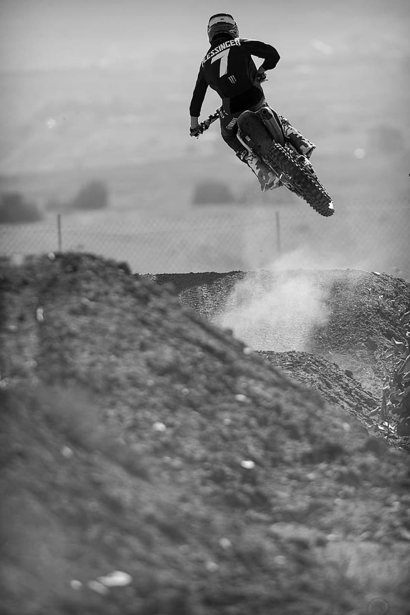 Motocross rider wearing number seven jumps a dirt bike mid-air while kicking up dust in a black and white photo.