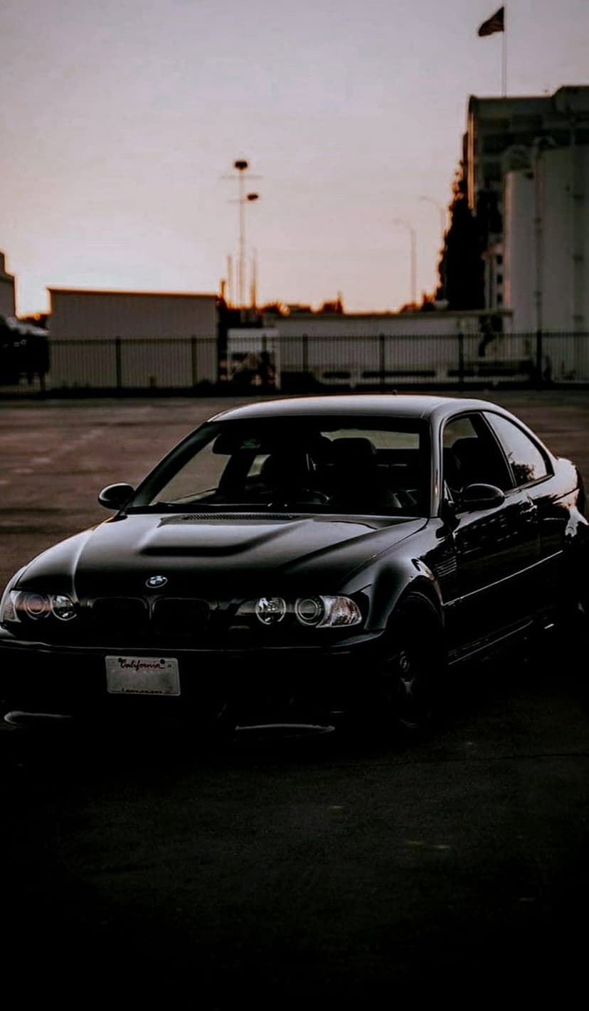 Black BMW M3 coupe parked on asphalt during a warm sunset with a California license plate on the bumper.