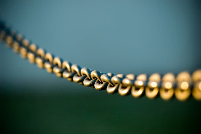 Golden metal chain links shimmer under warm sunlight against a soft blue and green blurred background.