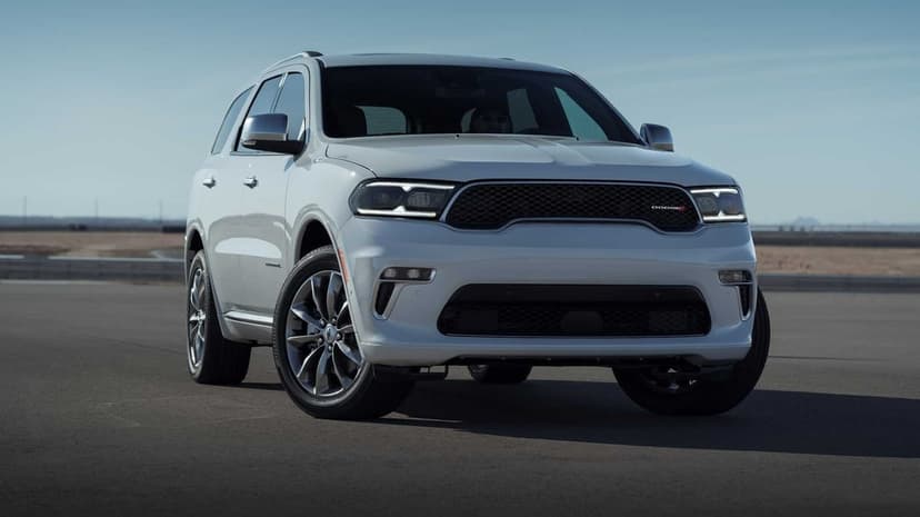 White Dodge Durango SUV parked on a flat asphalt track under a clear blue sky in bright natural daylight.