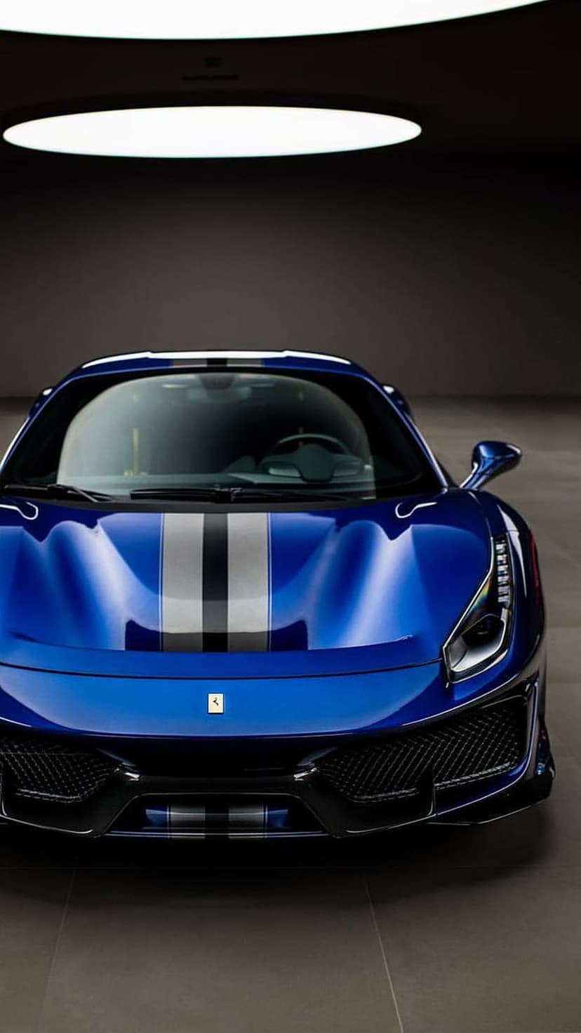 Blue Ferrari sports car with racing stripes on a polished studio floor under dramatic overhead lighting.