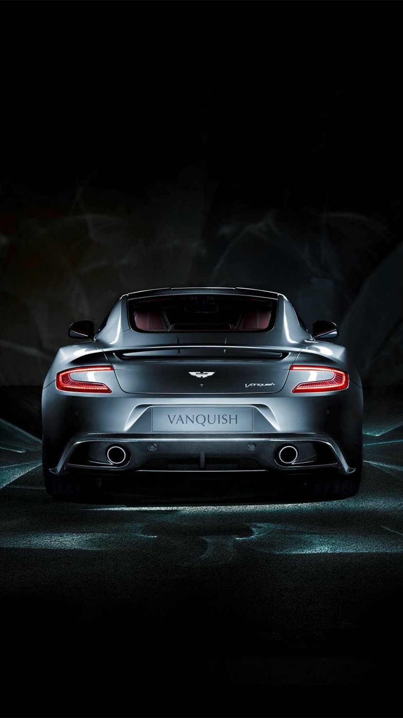 Aston Martin Vanquish rear view featuring glowing red LED taillights against a dark studio background.