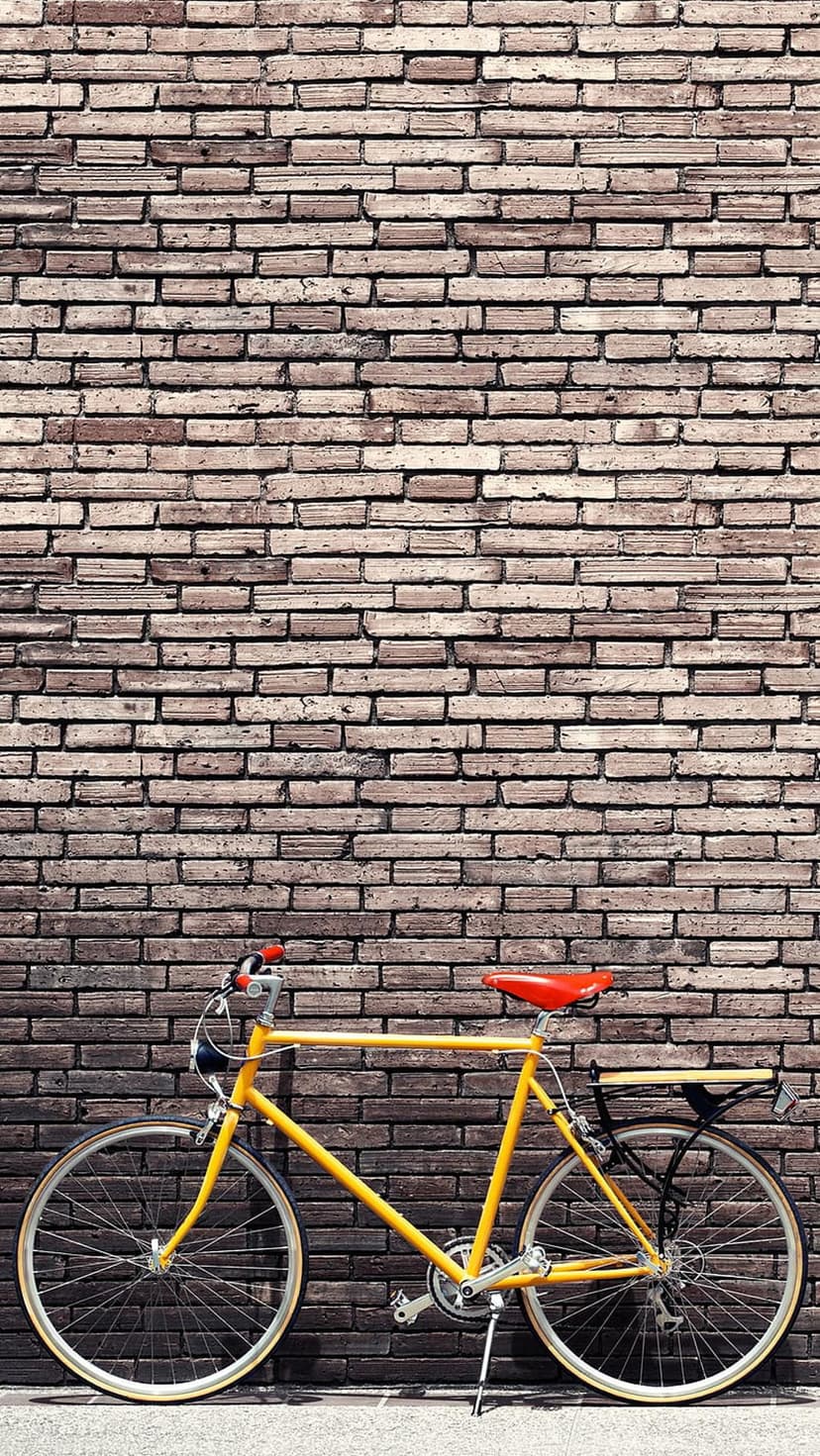 Yellow bicycle with a red saddle leaning on a weathered brick wall in a vertical street photography shot.