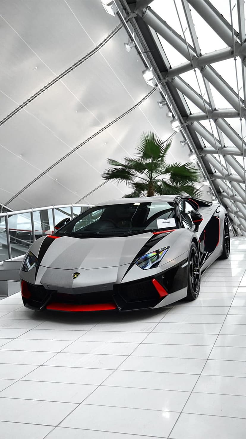 Lamborghini Aventador SVJ in silver with red highlights parked on a white tile floor inside a modern showroom.
