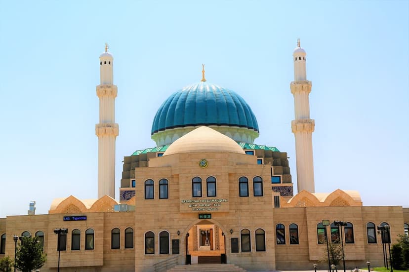 Ornate blue dome mosque with twin minarets and arched windows stands against a clear, sunny sky in midday light.
