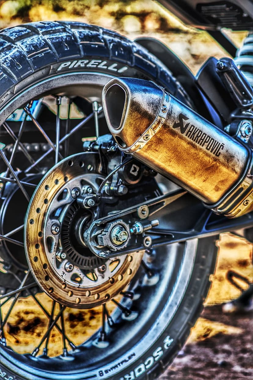 Akrapovič exhaust pipe and Pirelli tire tread on a spoked motorcycle wheel with a vented metal brake disc.
